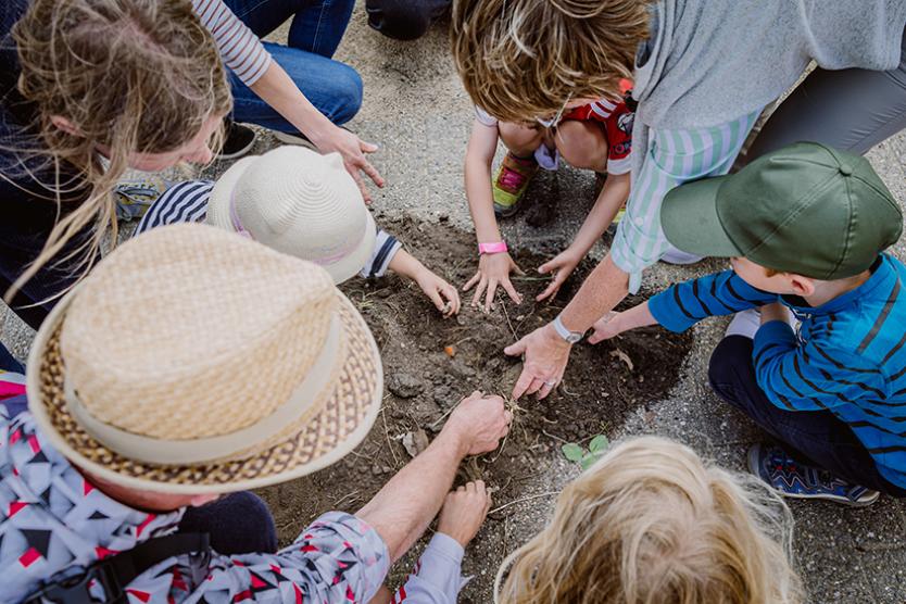 Eine Gruppe von Kindern und Erwachsenen kniet im Kreis und arbeitet gemeinsam an einer Stelle im Boden.