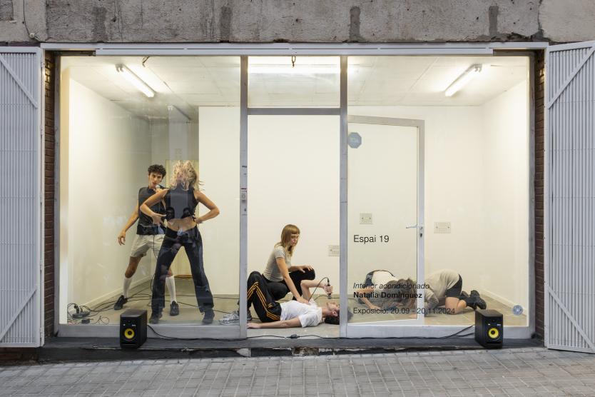 Eine junge Frau sitzt mit geschlossenen Augen auf dem Boden eines Studios und hält ein Mikrofon mit beiden Händen, während sie sich auf den Klang konzentriert – umgeben von Kabeln, Technik und minimalistischer Ausstattung.